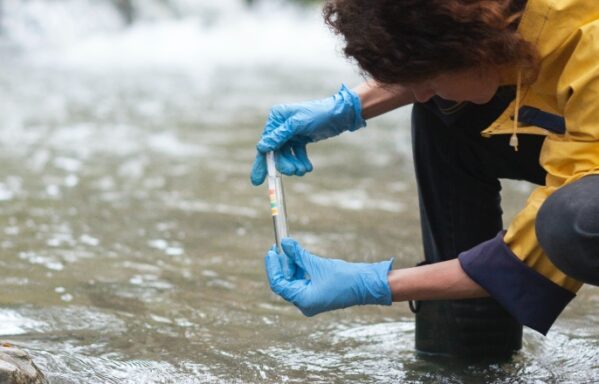 Registered Environmental Technician in a yellow coat taking a sample of water from a river society for the environment