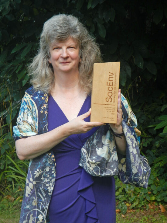 Claire holding SocEnv Award trophy in front of a green landscape